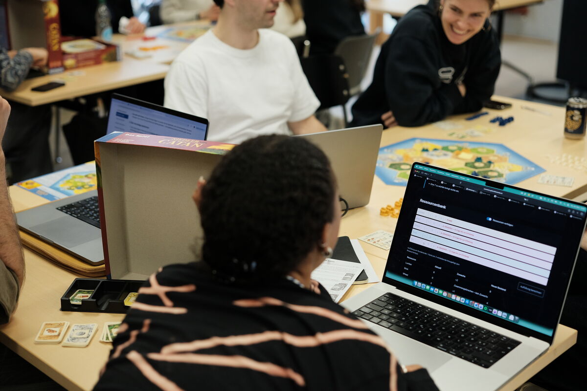 People playing board game, three laptops shown